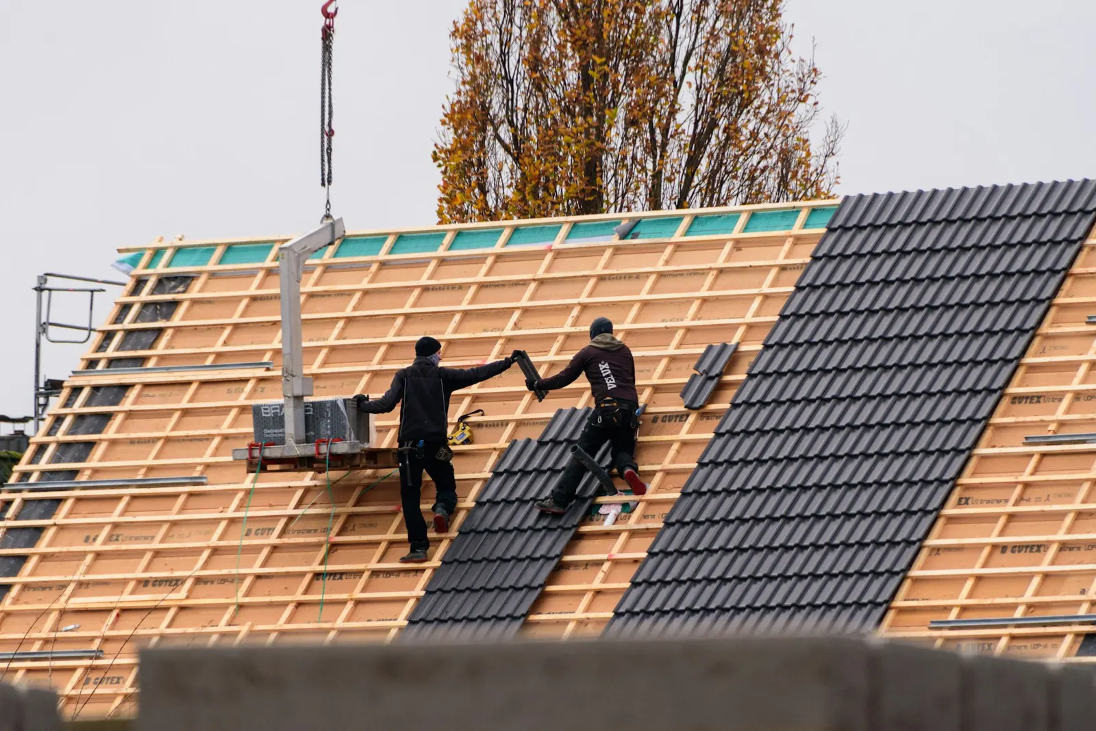 Couvreurs posant des tuiles sur la charpente d’une maison neuve