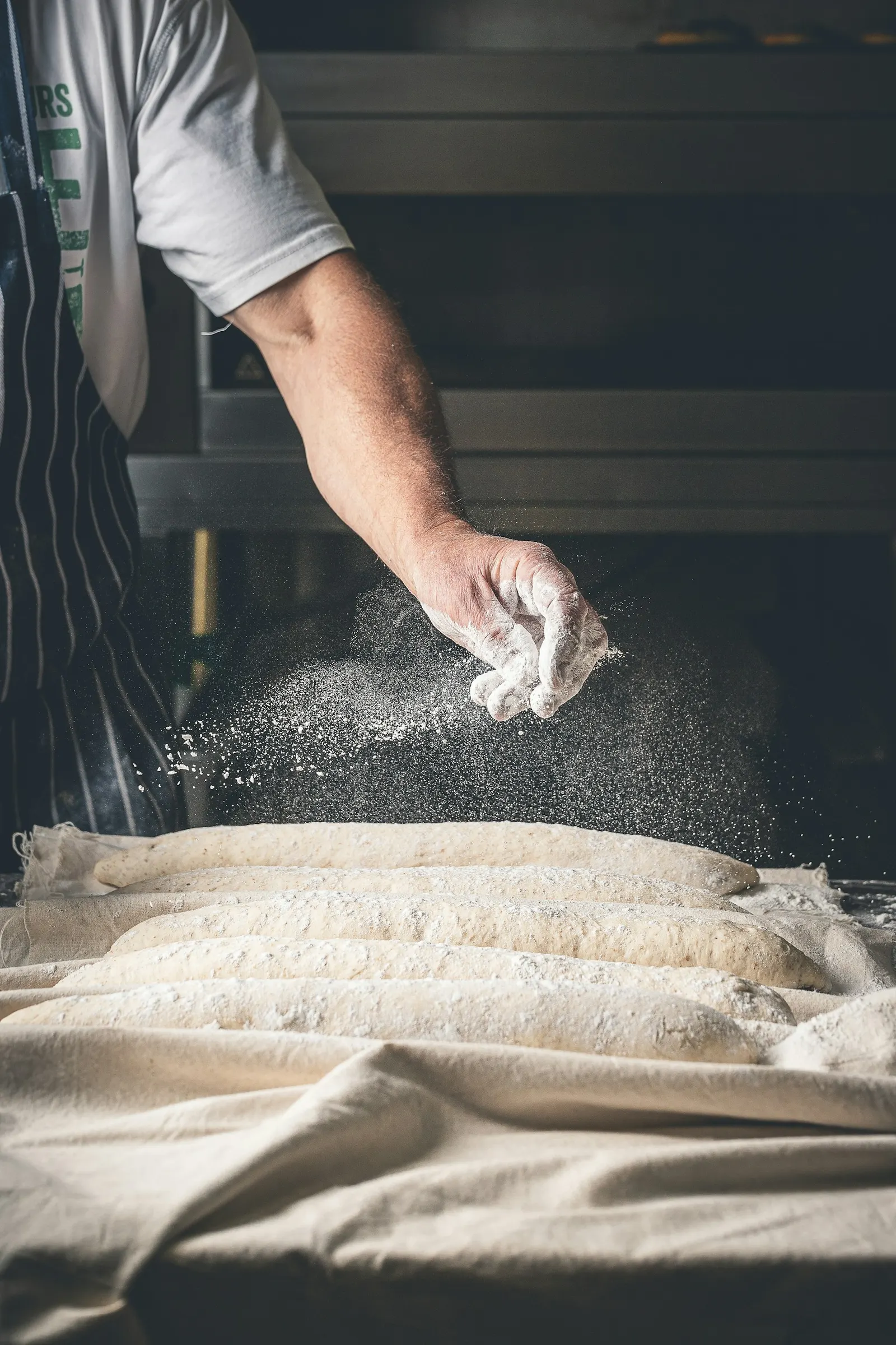 Boulanger saupoudrant de farine des pâtons sur le plan de travail