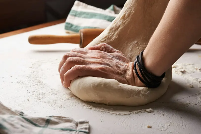 Mains pétrissant une pâte à pain sur un plan fariné