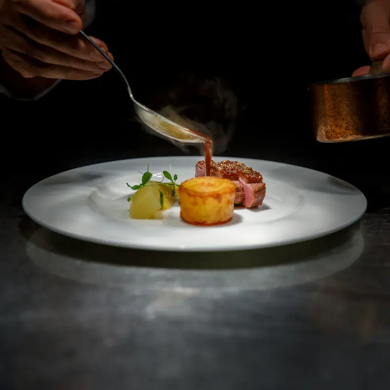 Chef versant une sauce sur une assiette dressée