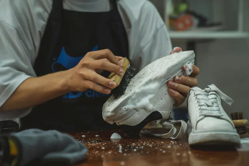 Artisan nettoyant une paire de baskets blanches