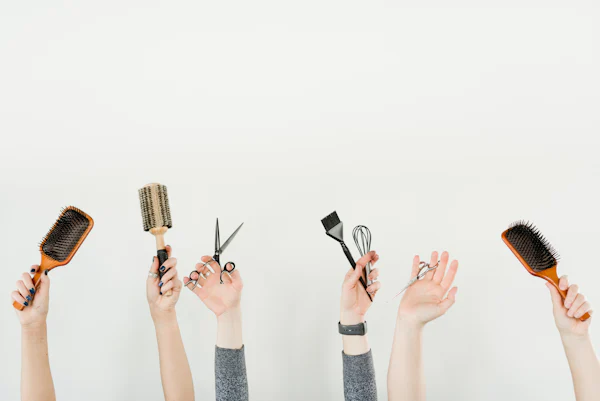 Mains tenant des ciseaux, des brosses et des peignes de coiffeur, illustration pour le site internet d’un salon de coiffure